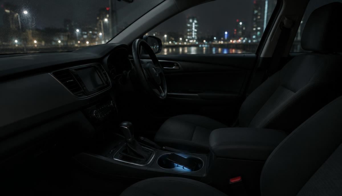 Interior de un auto vacío de noche, con un teléfono encendido en el portavasos y luces de la ciudad al fondo