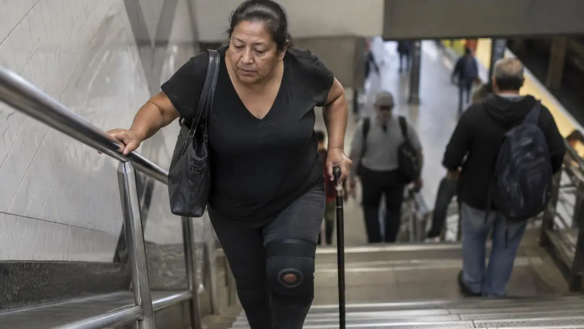 Mujer latina de mediana edad con rodillera y bastón subiendo las escaleras de una estación del metro de Nueva York Mujer latina de mediana edad con rodillera y bastón subiendo las escaleras de una estación del metro de Nueva York